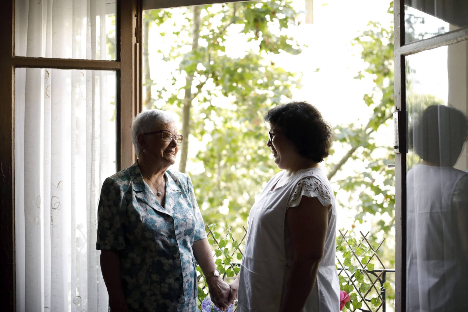 Persona en situación de dependencia hablando con una cuidadora en una ventana